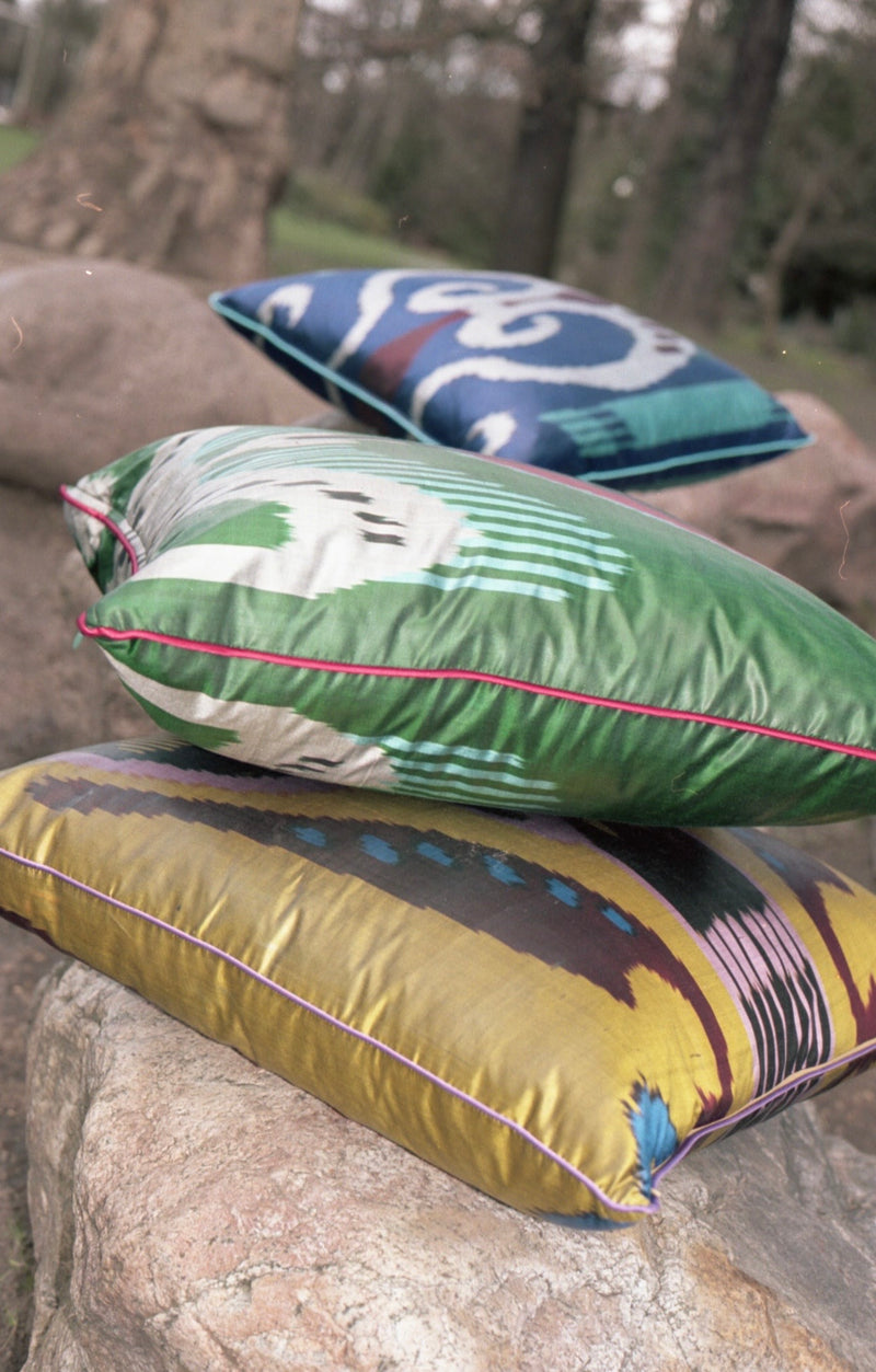 Gesa, Celena, and Ophelia ikat silk pillow cases stacked on a rock outdoors